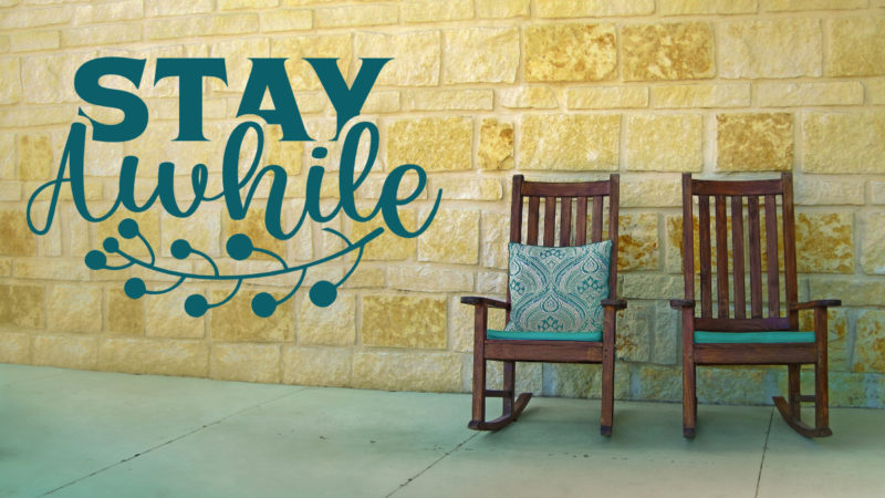 Two rocking chairs in front of a brick wall with the text "stay awhile" to the left